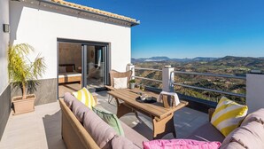 A balcony with wicker furniture, a table, and a view of the countryside.