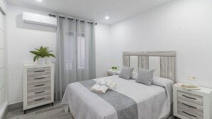 Un dormitorio con cama, mesitas de noche, armario, planta en maceta y equipo de aire acondicionado.
