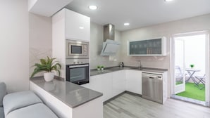 Una cocina moderna con horno empotrado, microondas y lavavajillas, encimera gris y una pequeña zona de comedor con mesa y sillas.