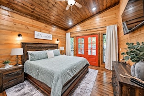A wooden cabin bedroom with a bed, nightstands, a red door, and a ceiling fan.