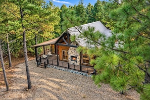 A cabin with a stone fireplace, wooden deck, and surrounded by pine trees.