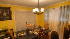 A dining room with a black table set for four, wooden chairs, a chandelier, and a door in the background. - Charming 3-bedroom house with AC and WiFi in peaceful Rockingham (Rockingham)
