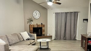 Una sala de estar con sofá, una mesita redonda, chimenea y ventilador de techo.