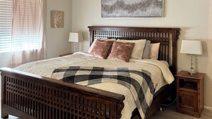 Un dormitorio con cama de madera, ventilador de techo, mesita de noche, lámpara y un cuadro en la pared.