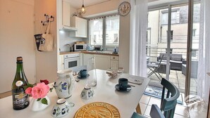 A modern kitchen with white cabinets, a microwave, and a dining area with a table set for two. - Le Duplex du Linkin - PERROS GUIREC (PERROS GUIREC)