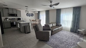 A modern living room with a sofa, a dining area, and a kitchen. - New Construction with Heated Swim Spa 5,5 mi to the beach with fenced back yard (Port Charlotte)