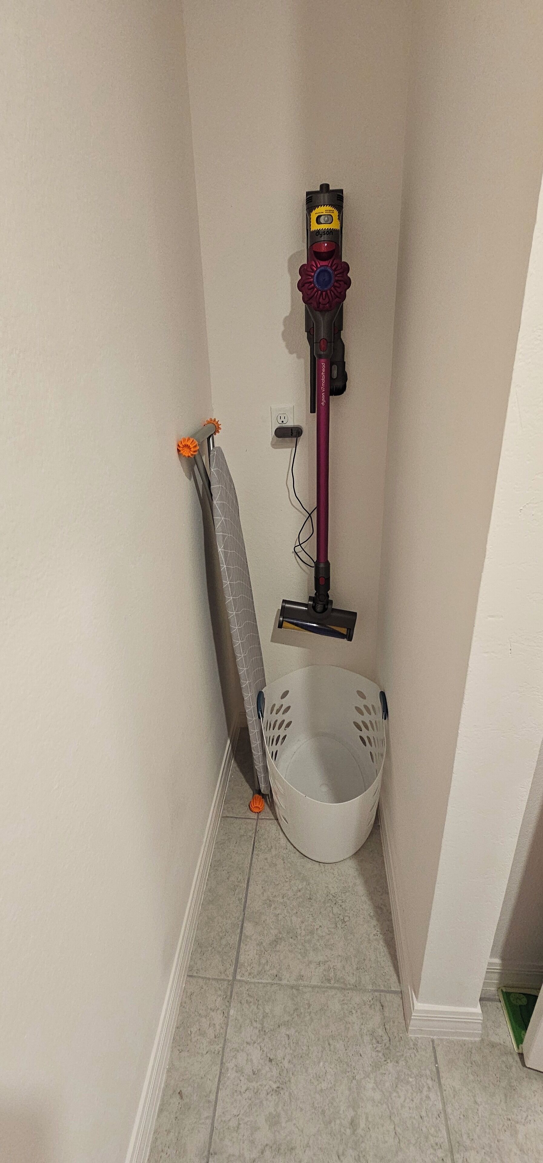Un coin de pièce avec un aspirateur, une planche à repasser et un panier à linge.