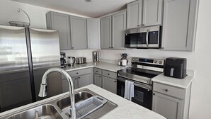 A modern kitchen with stainless steel appliances, grey cabinetry, and a built-in oven. - New Construction with Heated Swim Spa 5,5 mi to the beach with fenced back yard (Port Charlotte)
