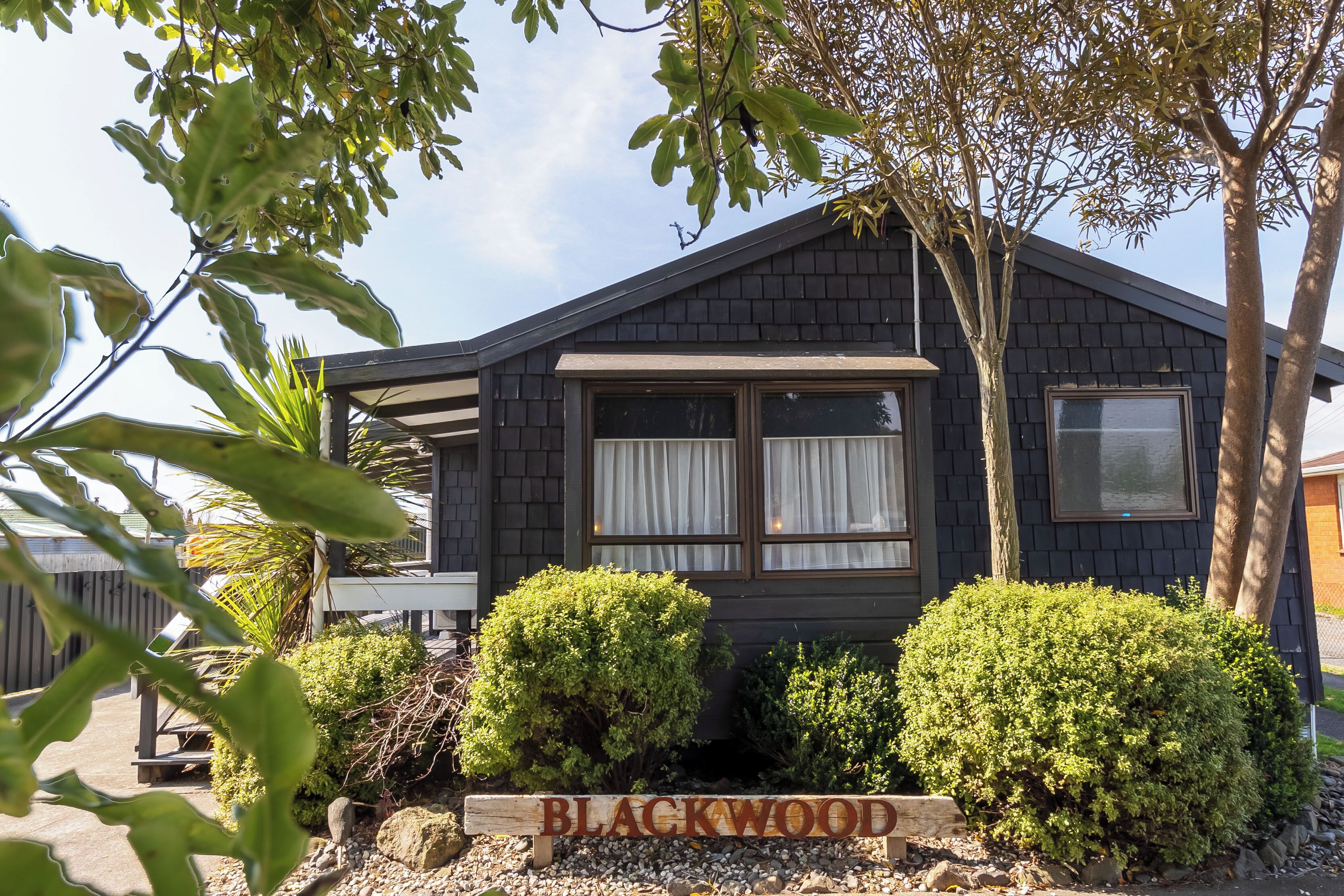 A house with a sign reading 'BLACKWOOD' in front, surrounded by well-maintained bushes and trees.
