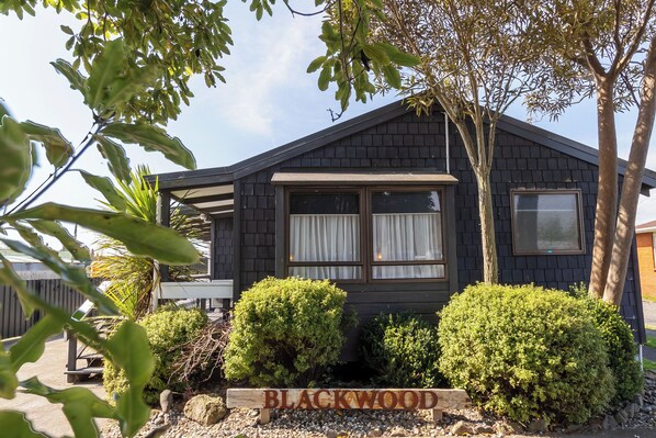 A house with a sign reading 'BLACKWOOD' in front, surrounded by well-maintained bushes and trees.