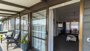 Un espacio exterior cubierto con un gran ventanal corredizo que da a una habitación con una cama, un escritorio y una silla.