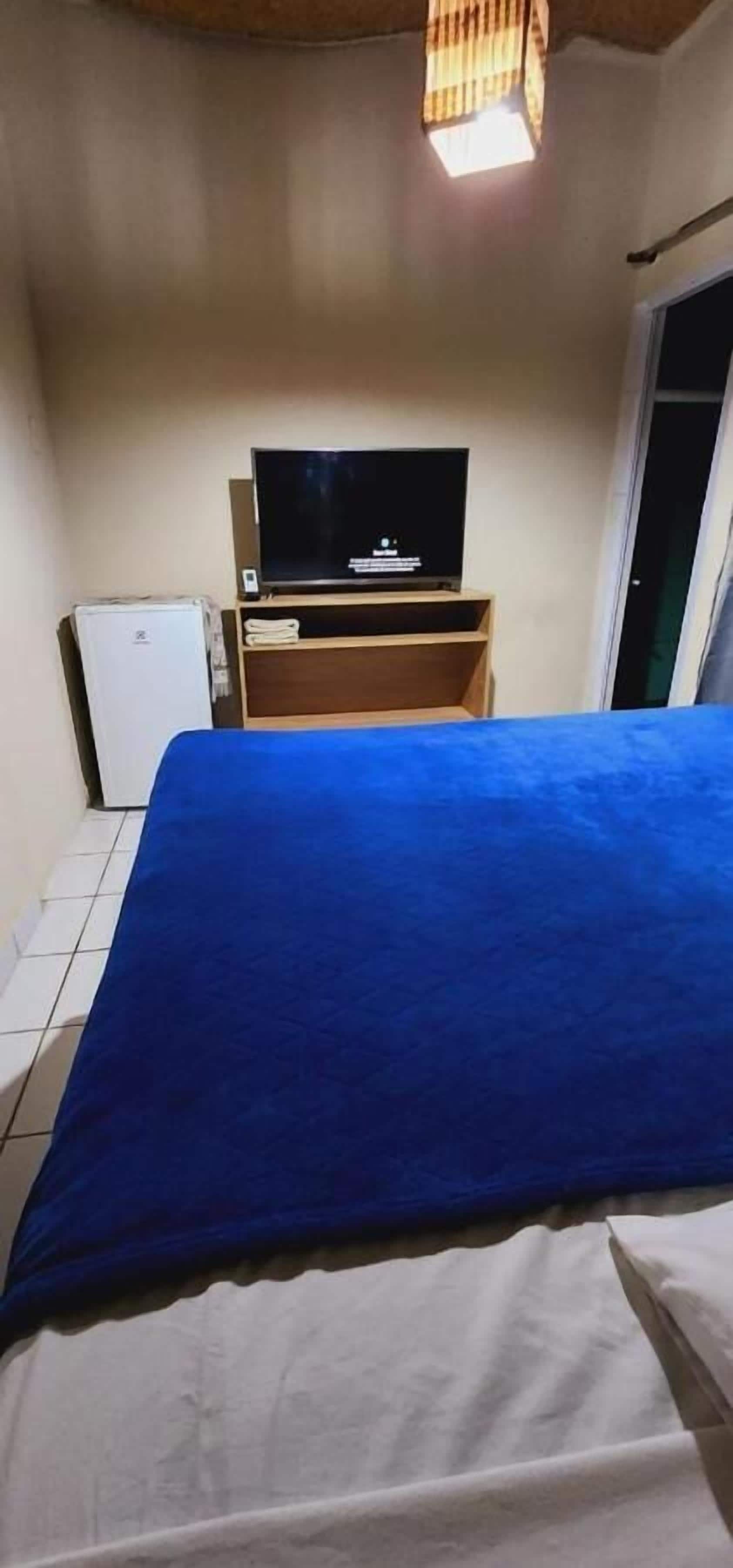 A room with a bed, a television on a wooden stand, and a white refrigerator.