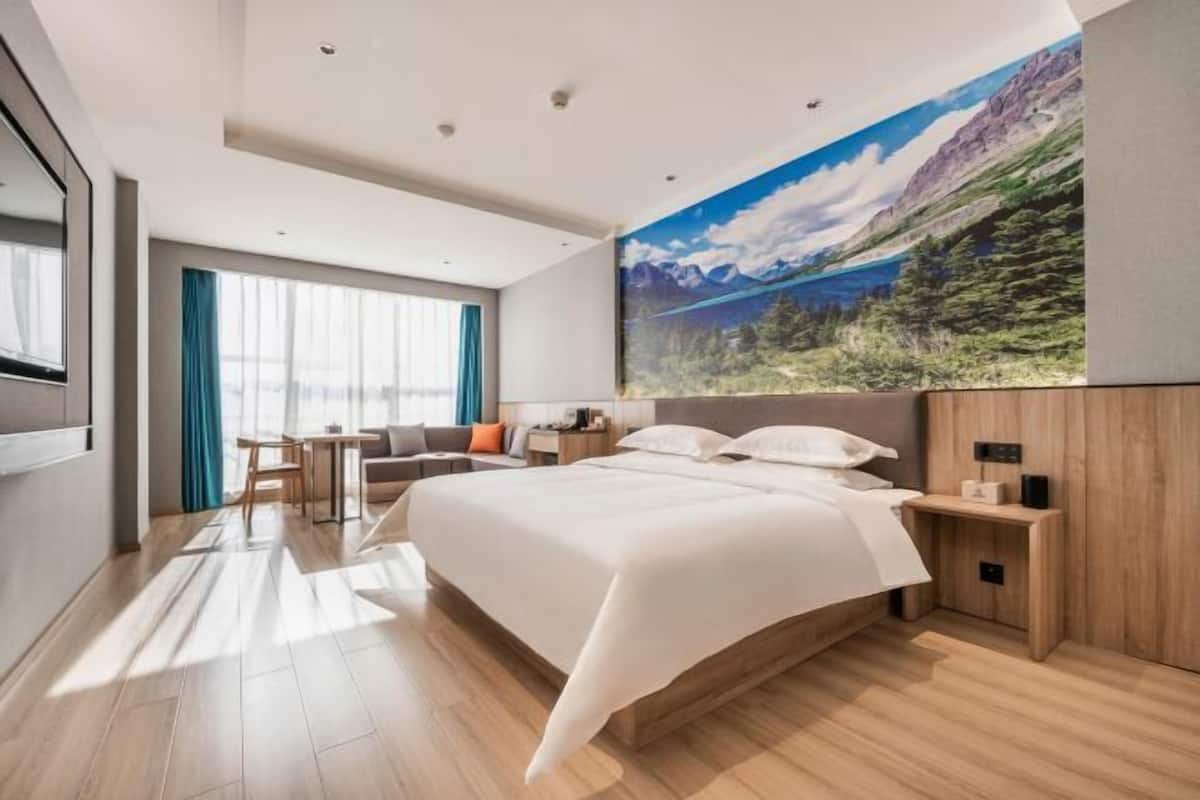A modern hotel room with a large bed, a desk, a chair, and a view of a mountain landscape.