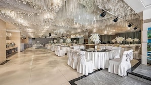 Un salón amplio con mesas redondas y sillas blancas, techo alto con decoraciones colgantes y suelo de mármol.