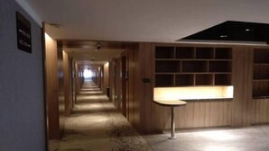 A hotel corridor with wooden paneling, a patterned carpet, and a small table with a lamp. - Yulin Polentino Hotel (Railway Station Branch) (Yulin)