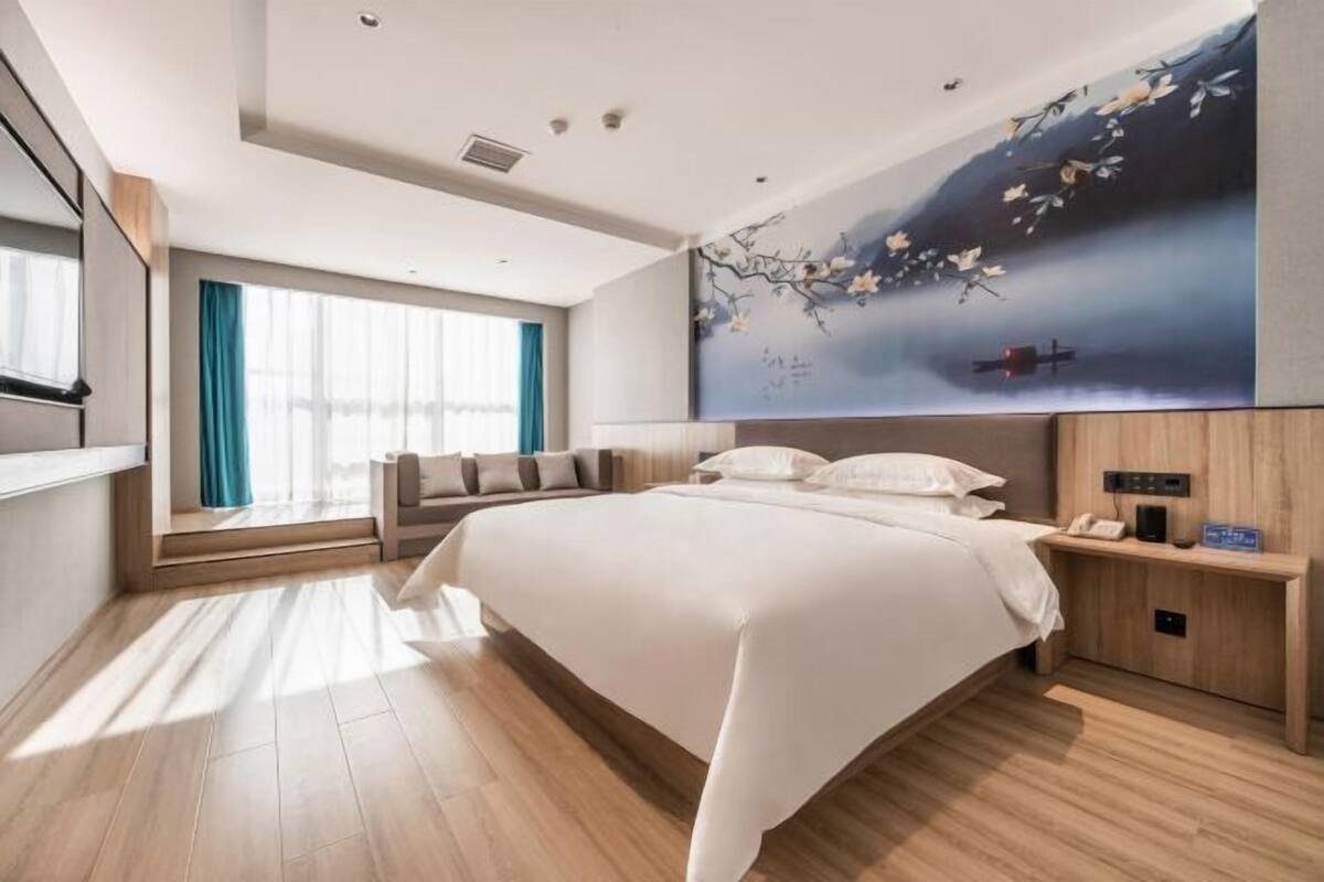 A modern hotel room with a large bed, a nightstand with a phone, and a wall mural.