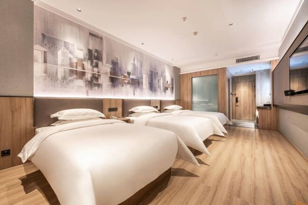 A hotel room with three beds, a large abstract painting on the wall, wooden flooring, and a modern design.