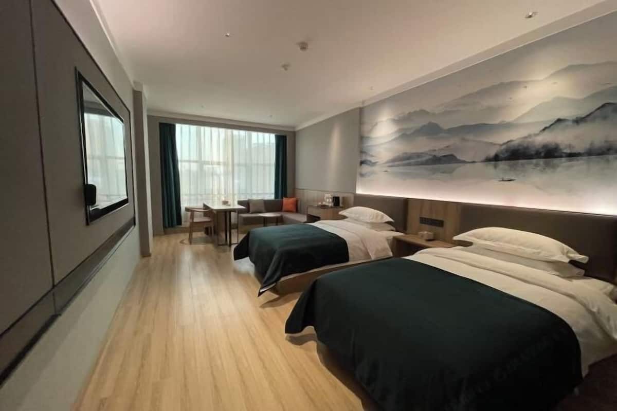 A hotel room with two beds, a desk, a chair, a large window, and a wall-mounted painting.