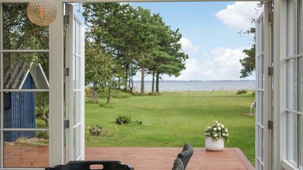 An open door leading to a deck with a view of a grassy area and trees, a small shed, and a potted plant. - 3 bedroom beautiful home in Thyholm (Thyholm)