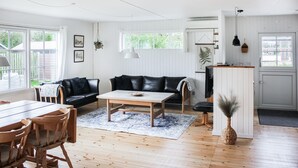 A spacious living room with a black leather sofa, wooden coffee table, and a dining area with wooden chairs. - 3 bedroom beautiful home in Thyholm (Thyholm)
