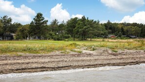 A coastal landscape with a sandy beach, a grassy field, and a row of houses in the background. - 3 bedroom beautiful home in Thyholm (Thyholm)