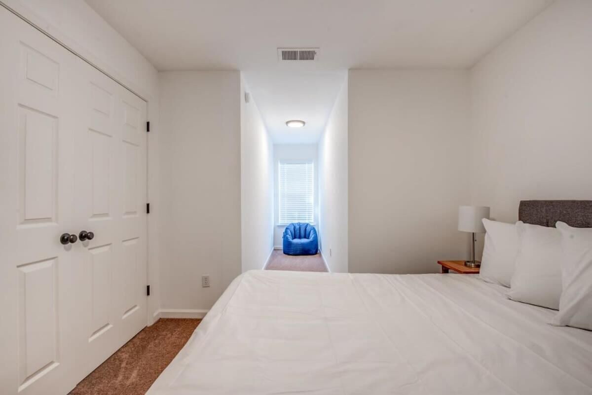 A bedroom with a large bed, a nightstand with a lamp, a blue bean bag chair, and a door with a window above it.