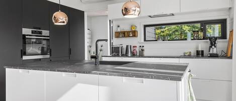 A modern kitchen with a central island, built-in oven, and pendant lighting.