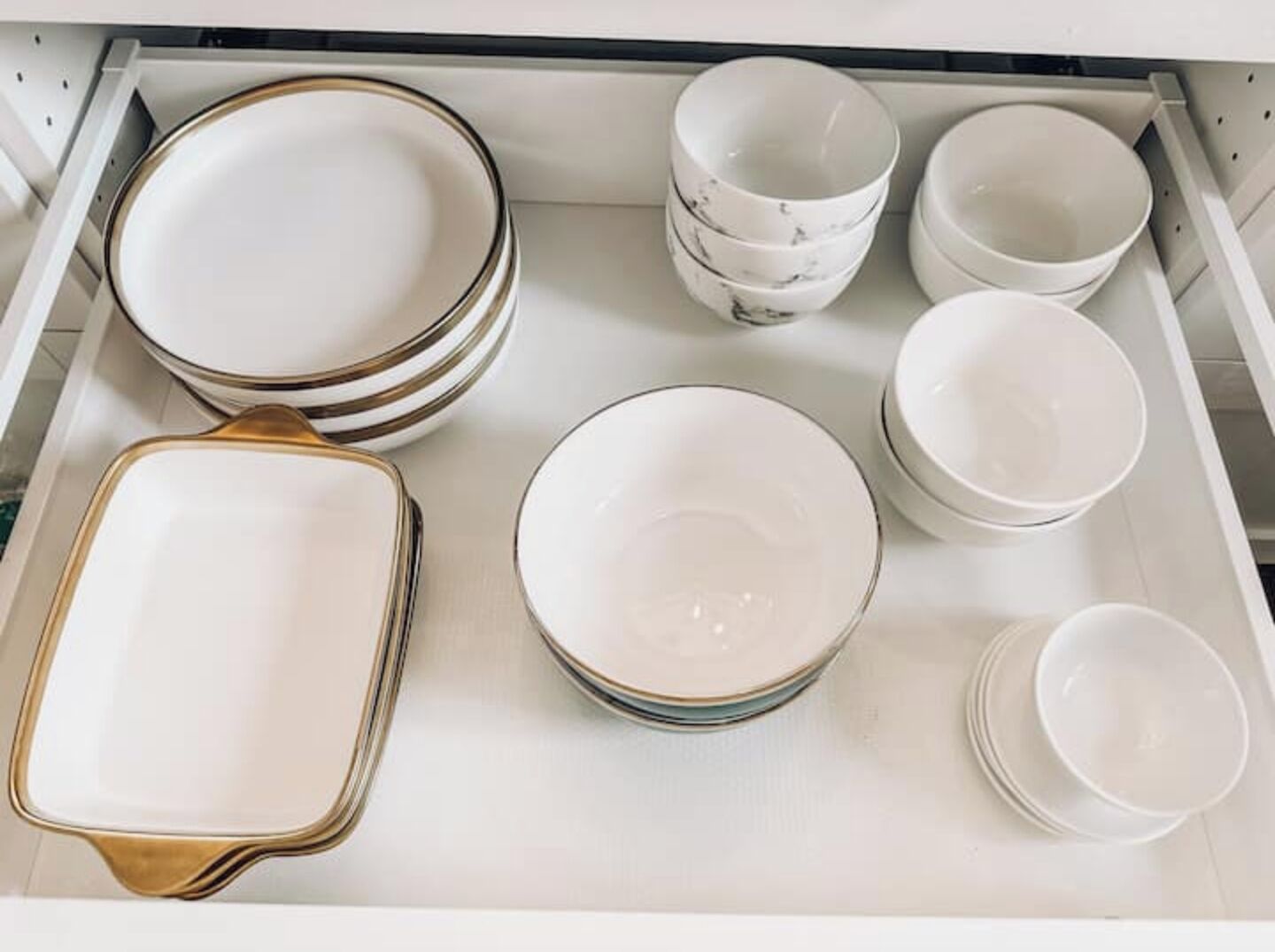 A drawer containing various white ceramic dishes and a gold-trimmed serving tray.