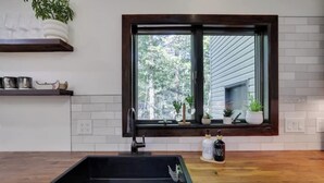 A kitchen with a black sink, wooden countertop, and a window with a view of trees. - King David Luxury getaway (Blakeslee)