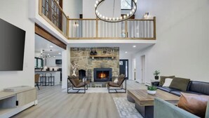 A spacious living area with a stone fireplace, a high ceiling, and a balcony. - King David Luxury getaway (Blakeslee)