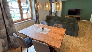Un salón acogedor con una mesa de comedor de madera, un sofá tapizado en gris y un televisor sobre una pared verde.