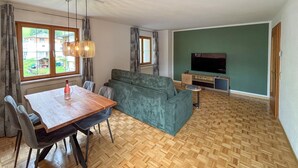 Una sala de estar moderna con una mesa de comedor de madera, un sofá gris y un televisor sobre una pared verde.