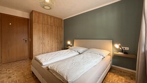 Un dormitorio con cama doble, armario de madera, mesitas de noche con lámparas y suelo con estampado de espiga.