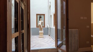 An open doorway leading to a courtyard with a statue, wooden flooring, and a radiator. - House Bacco (Firenze)
