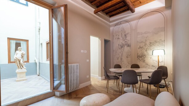 A modern dining area with a round table and chairs, a statue outside, and a large window. - House Bacco (Firenze)