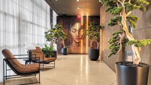 A lobby with a modern design, featuring a large potted tree, seating area, and a wall with a large portrait. - Luxury 1BD Penthouse • Bay & City Views • Downtown Miami (Miami)