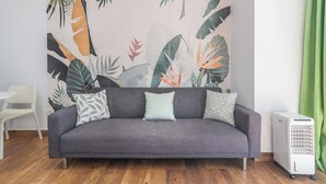 A grey sofa with patterned cushions, a white radiator, and a green curtain in a room with a tropical leaf-patterned wall.