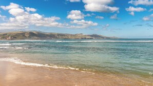 A beach with clear blue water, sandy shore, and distant hills.