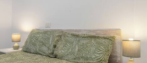 A bed with a patterned green bedspread, two bedside lamps, and a wooden headboard.