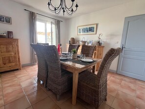 A dining area with wicker chairs, a wooden table, and a chandelier.