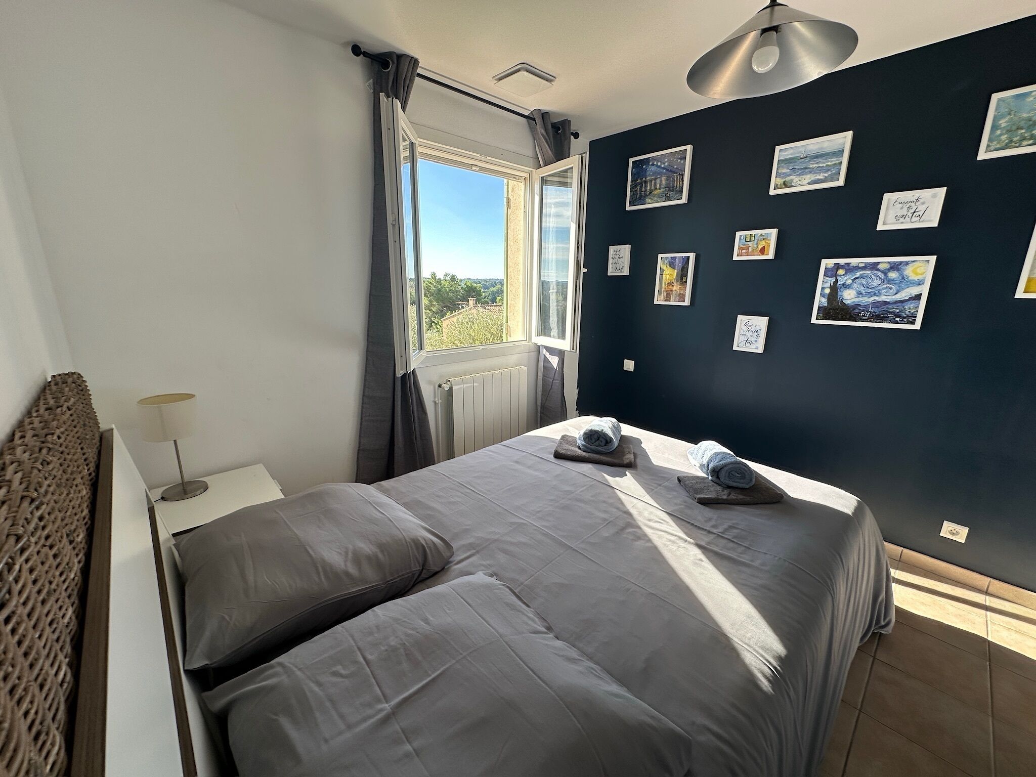 Une chambre avec un grand lit, une fenêtre avec des rideaux et un mur décoré de tableaux encadrés.