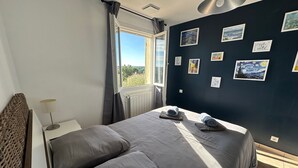 Ein Schlafzimmer mit einem großen Bett, einem Fenster mit Vorhängen und einer Wand, die mit gerahmten Bildern dekoriert ist.