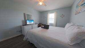 A bedroom with a bed, a desk, a ceiling fan, and a window.