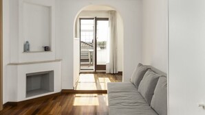A modern living room with a fireplace, a sofa, and a view through an archway to a balcony. - LaDolcevita - Ponte Milvio Stunning View Penthouse (Roma)
