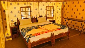 A traditional room with a bed, two windows, a nightstand, and a table. - Rajasthan Desert Camp  (Jaisalmer)