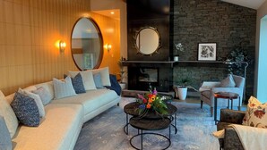 Un salon moderne avec un canapé, une table basse agrémentée de fleurs, une cheminée et un mur en pierre.
