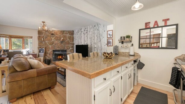 Eine moderne Küche mit einer Wand in Steinoptik, einer Kochinsel und einem Essbereich mit Sofa und Kamin.