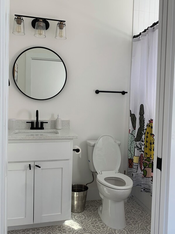 A bathroom with a white sink, mirror, and toilet. There are three light fixtures above the mirror and a metal bucket near the toilet. - Charming & Modern 2-Bedroom House Austin with AC, WiFi, & More (Austin)