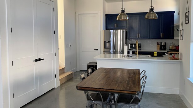 Una cocina moderna con armarios azul oscuro, electrodomésticos de acero inoxidable y una mesa de comedor de madera con sillas de metal.