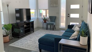 Una sala de estar con televisor, sofá, sillón y plantas en macetas.